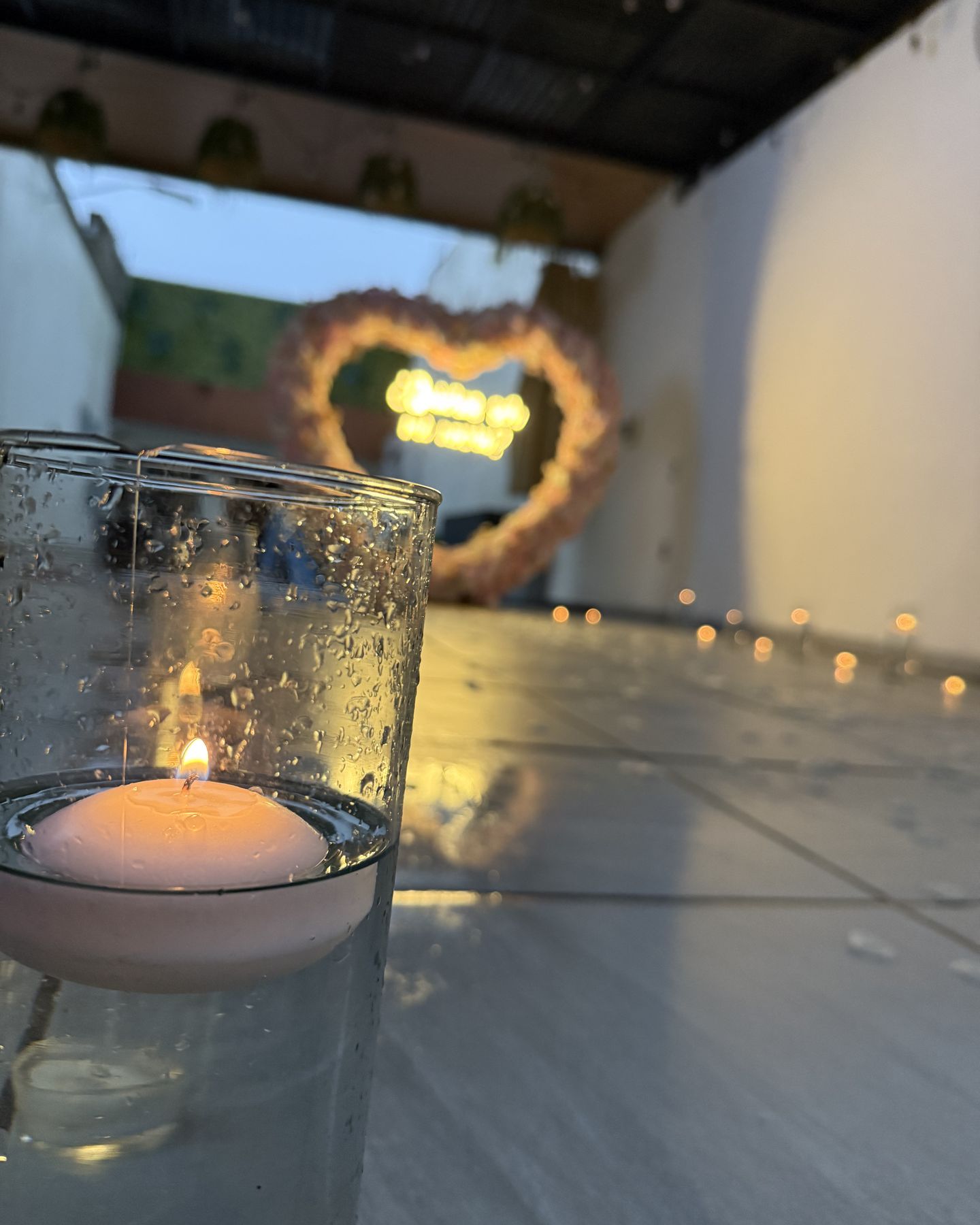 Una vela flotante encendida en la terraza de Terraza Plutarco de noche, con el corazón de flores iluminado al fondo, en Guadalajara
